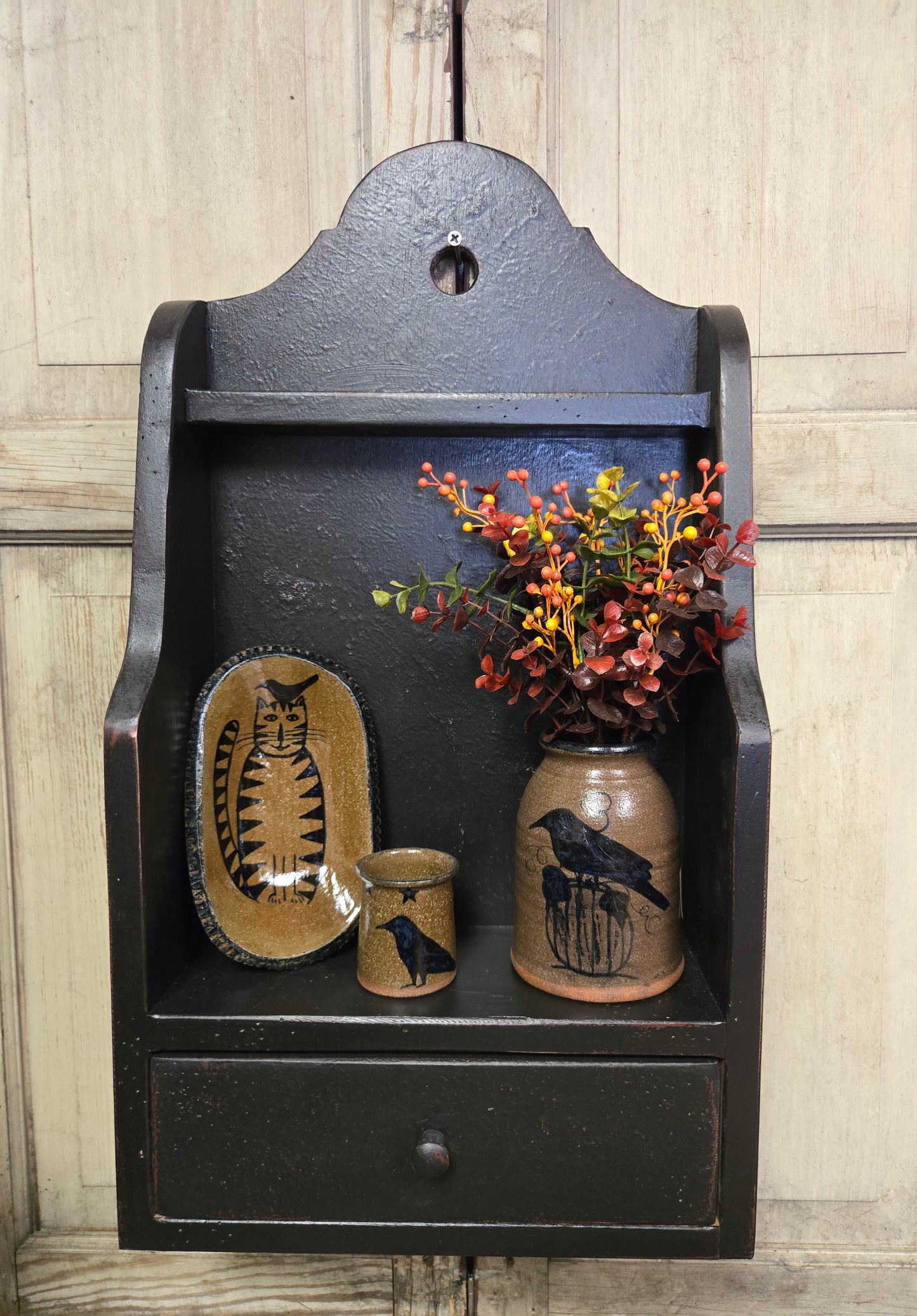 Decorative wall shelf with ceramic items and a vase of flowers against a wooden background