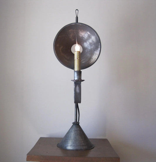 A vintage-style Cyrus Mini Mirrored Tin Table Light with a large reflective dish and a candle-like light source, placed on a wooden surface.
