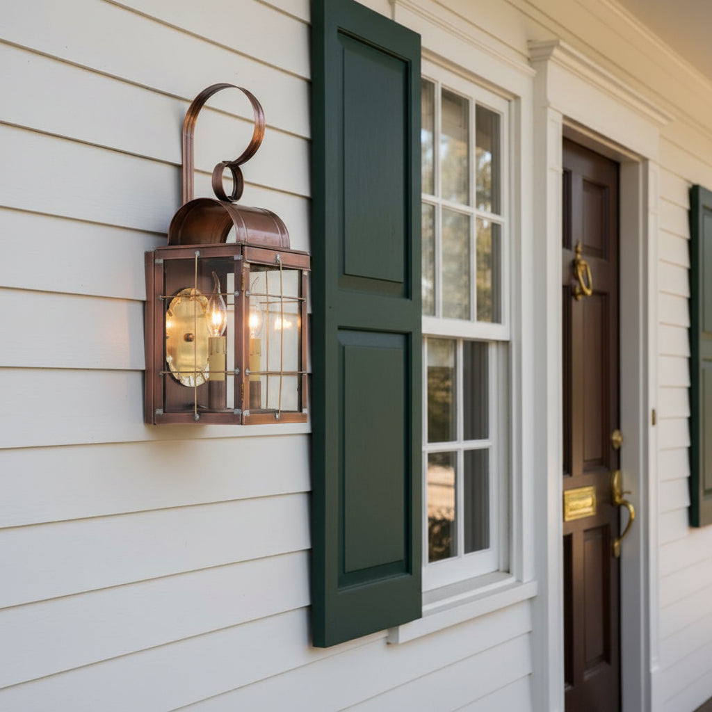 Antique copper double wall lantern with clear glass and brass hardware, mounted on colonial home beside front door.