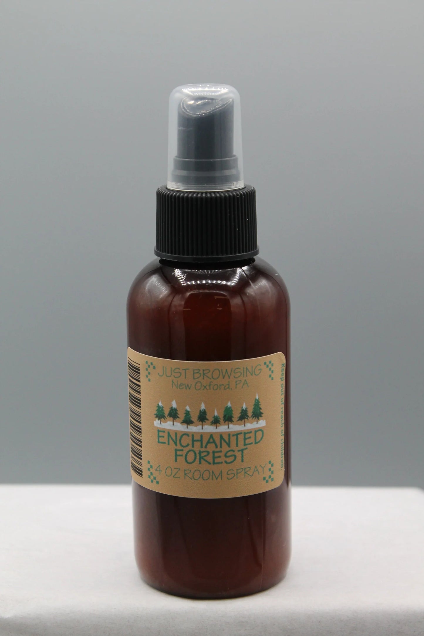 A 4oz bottle of Enchanted Forest room spray with a mist spray top. The bottle is brown with a label that has green text and a Christmas tree graphic, indicating a holiday-themed fragrance.