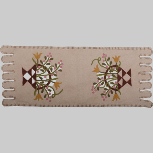 A cream-colored table runner with a floral basket design in the center, featuring embroidered details.