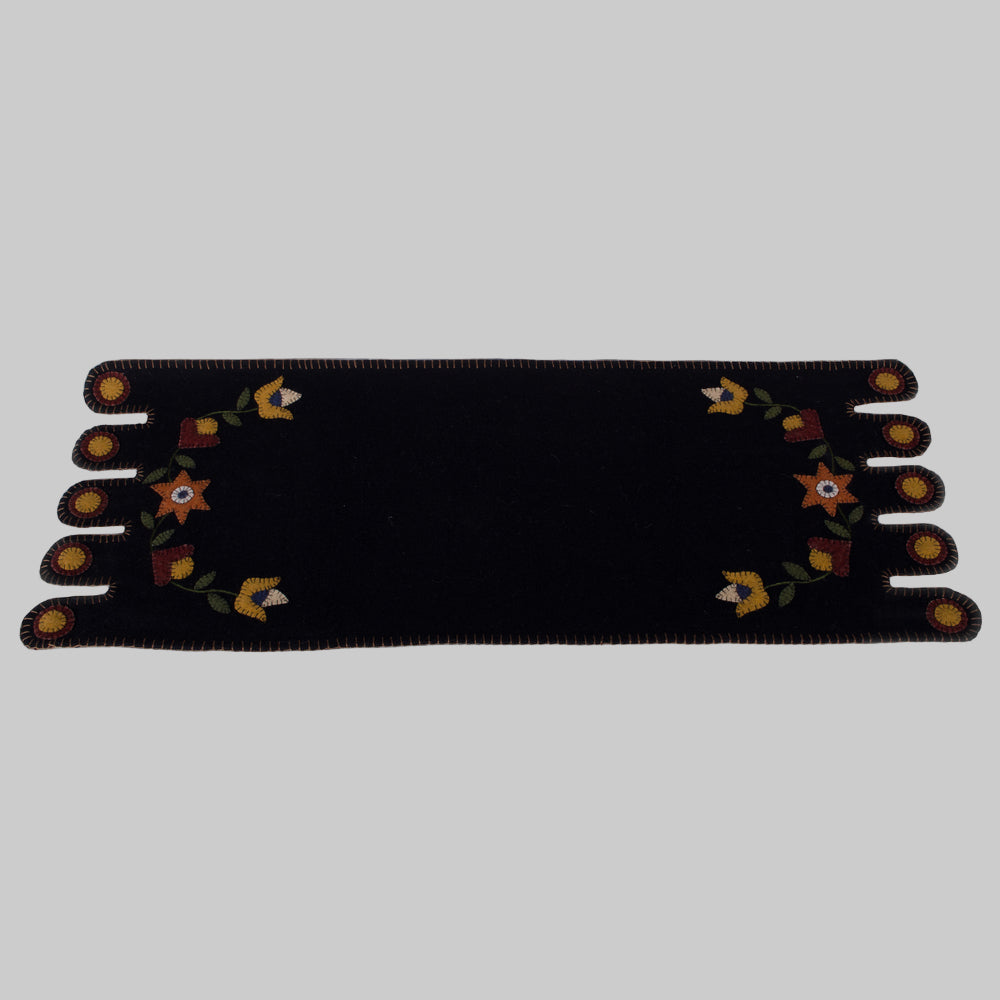 A black table runner with a floral design in the center, displayed on a neutral background.