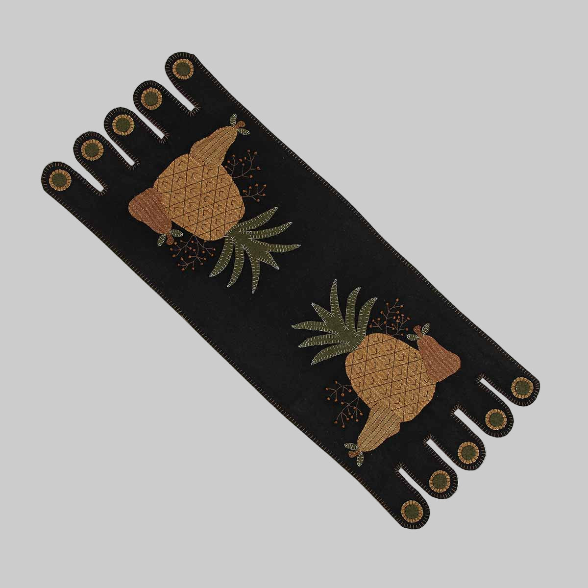 A black table runner with a folk art design featuring pineapples and tassels.