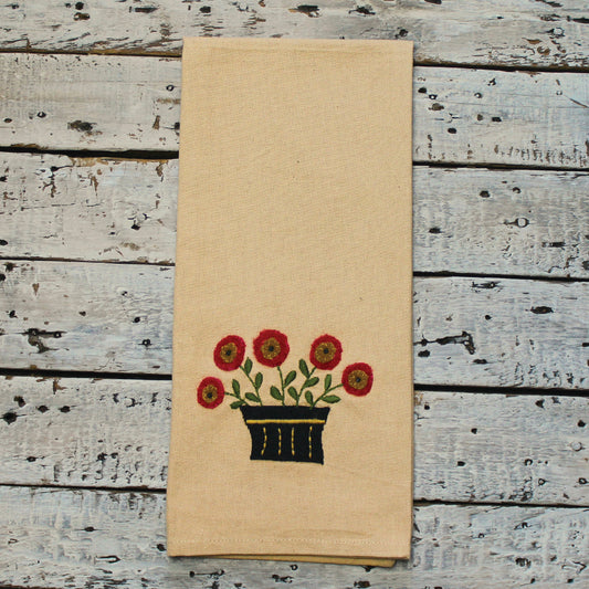 A beige cotton hand towel with a small, embroidered flower basket design in nutmeg-colored flowers.