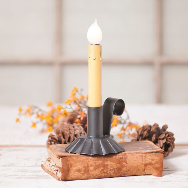 Decorative candle holder with a lit candle on a wooden base, surrounded by pinecones and autumn leaves.