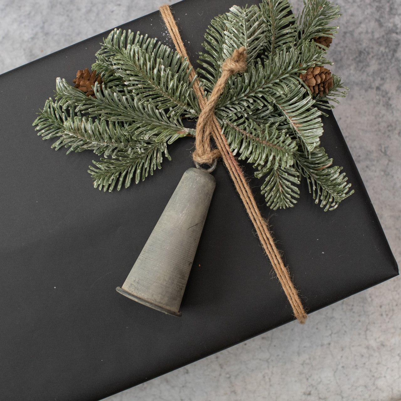 Galvanized large bell ornament on top of a black gift box with some greenery.