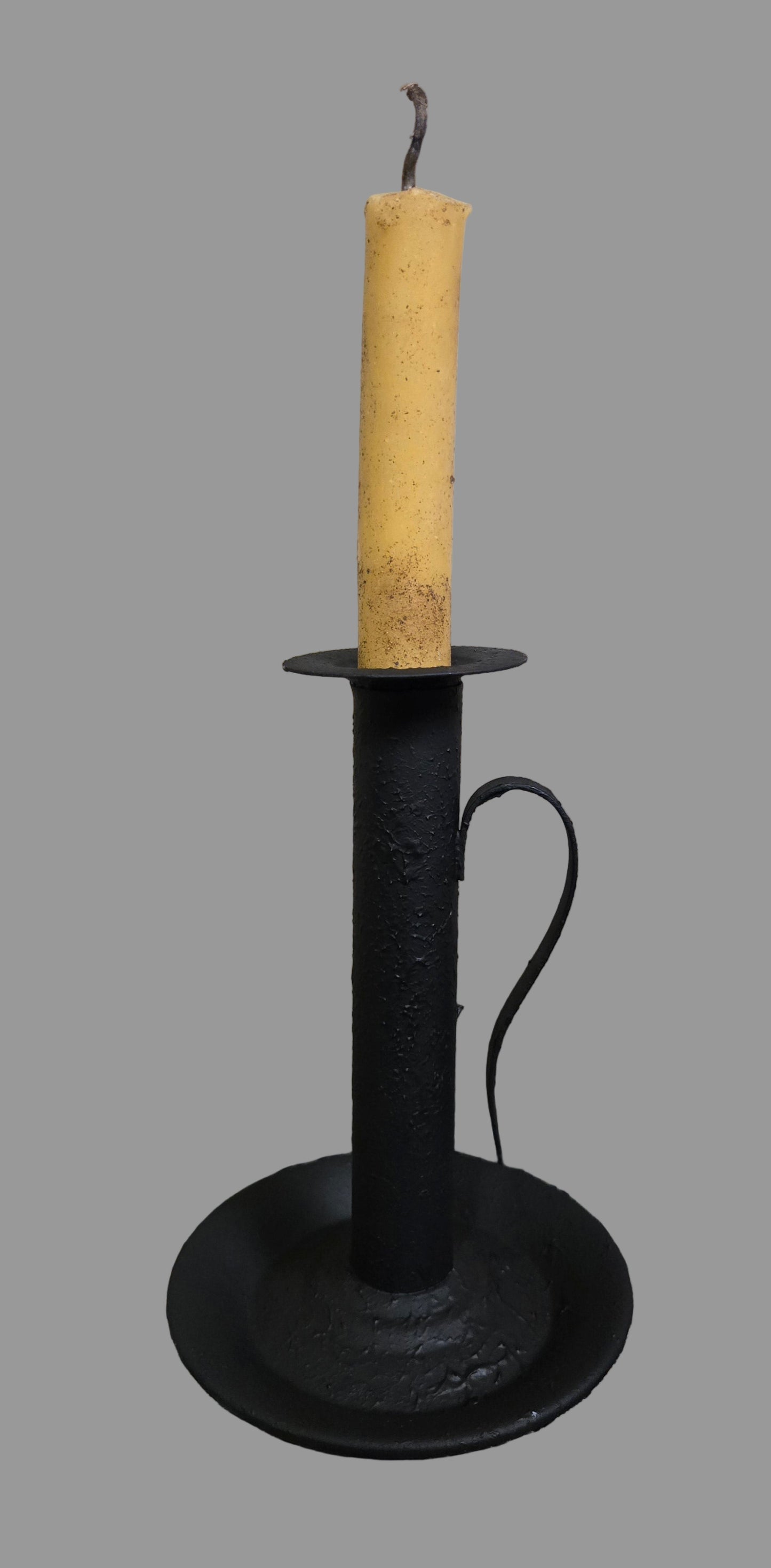 Black candle holder with a beige candle on a wooden surface, Christmas decorations in the background.