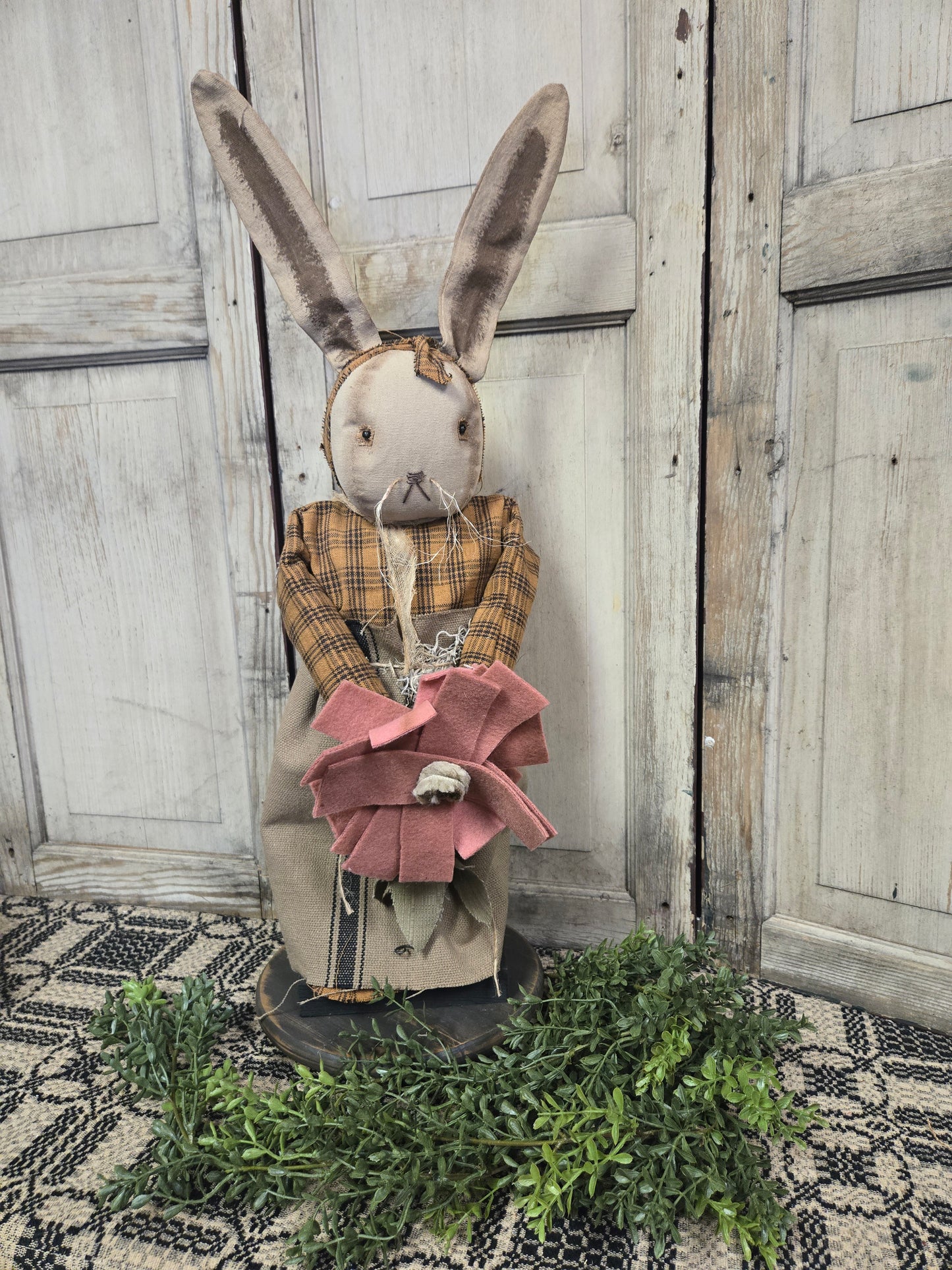 A handcrafted figurine of a primitive-style bunny with a floral design, dressed in a shirt and pants, standing against a rustic wooden backdrop.