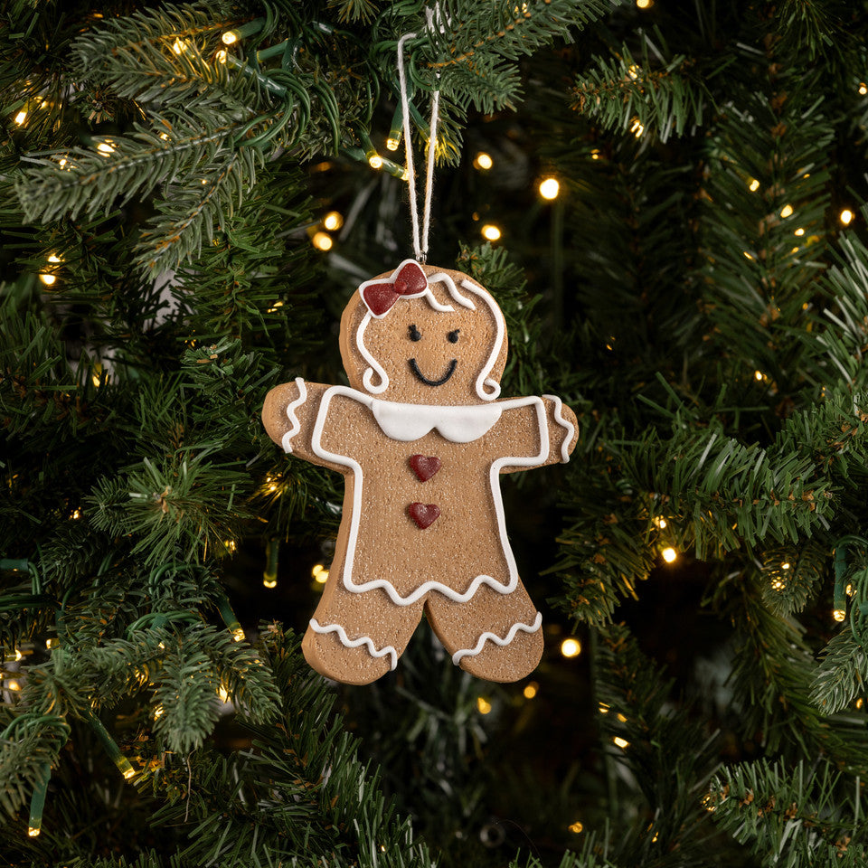 Gingerbread man ornament hanging on a Christmas tree with lights.