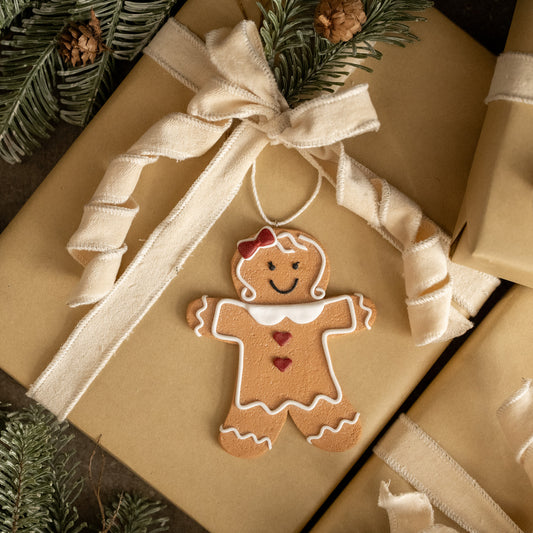 Gingerbread man ornament on a wrapped gift with a beige ribbon.
