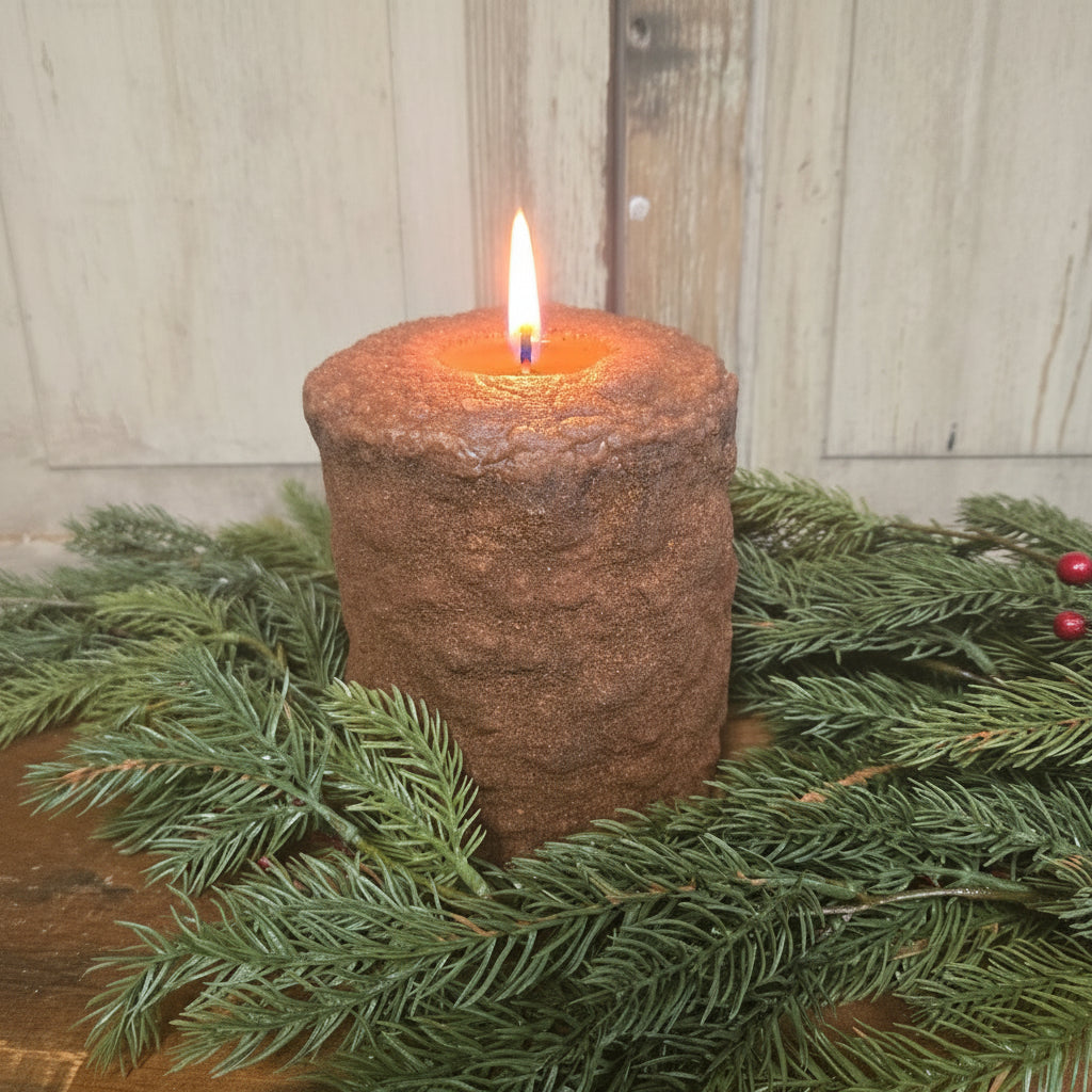 A large brown gingerbread spice latte candle on a wooden surface, surrounded by green pine branches and red berries.