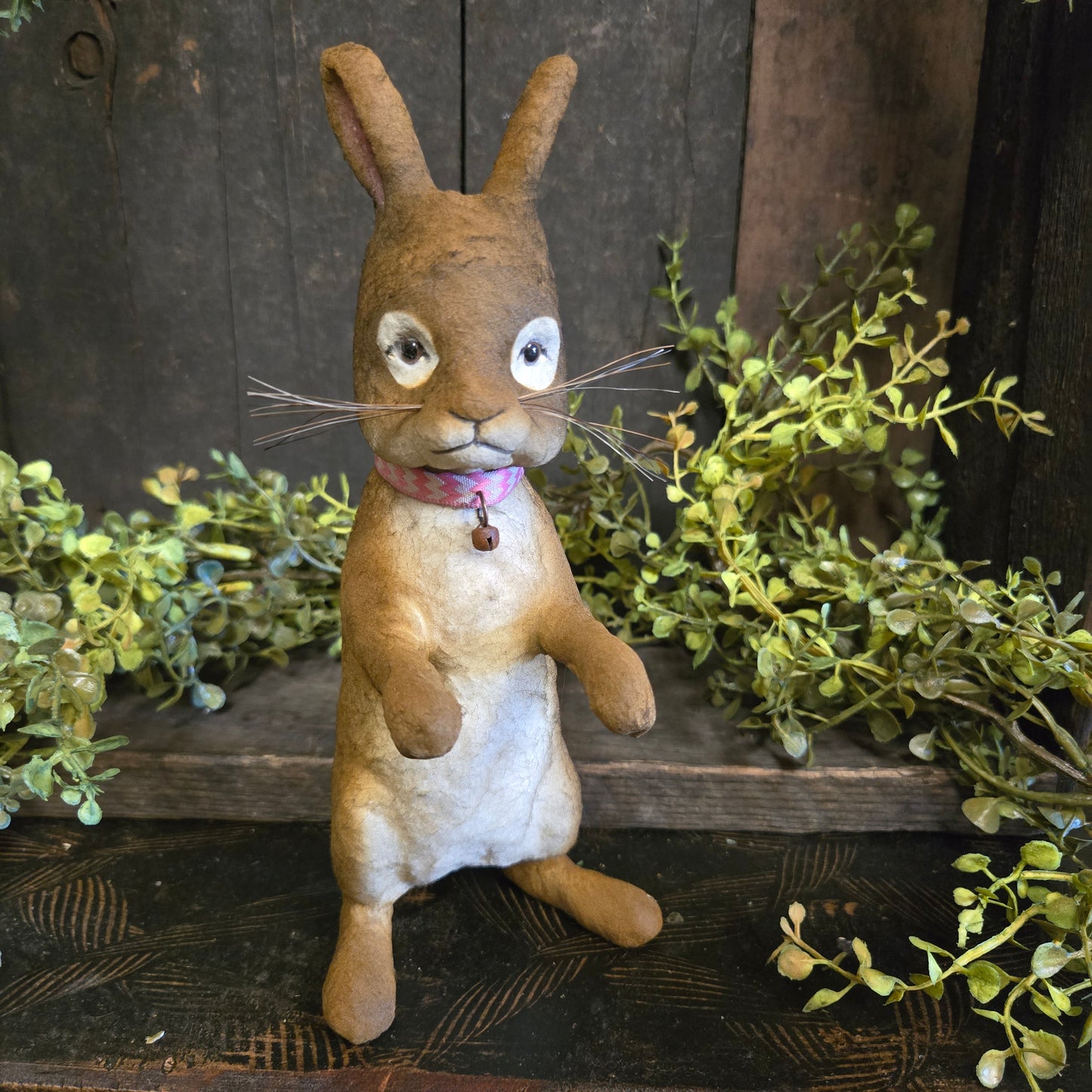 Vintage-style stuffed animal rabbit with greenery on a rustic wooden background