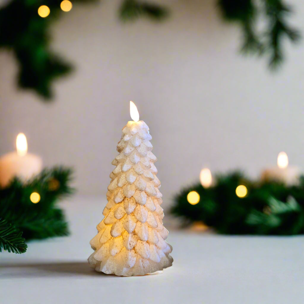 An LED tree-shaped candle with a burnt ivory color, illuminated to mimic a flame, placed on a table against a wooden background.