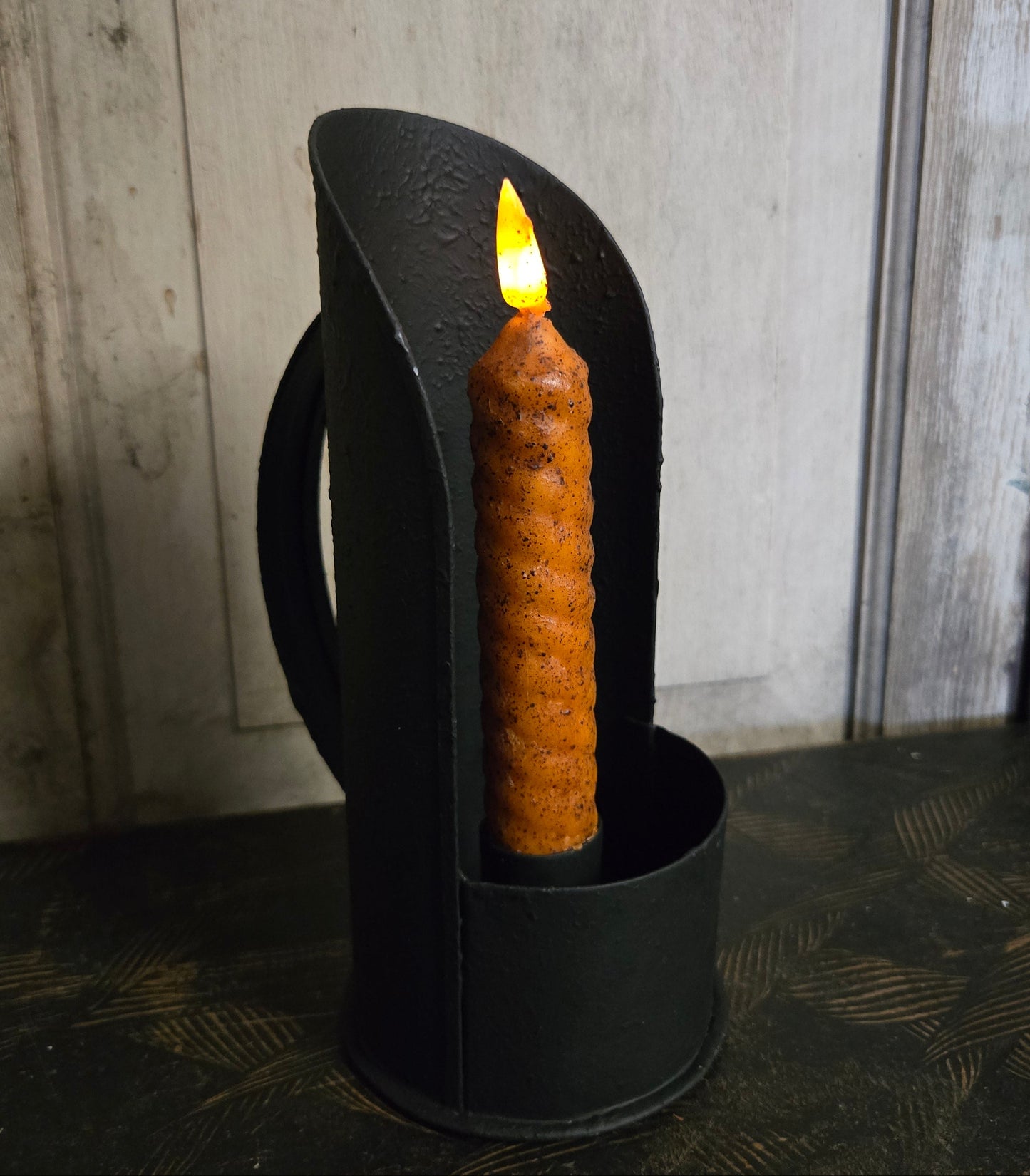 Black candle holder with a lit candle on a wooden surface