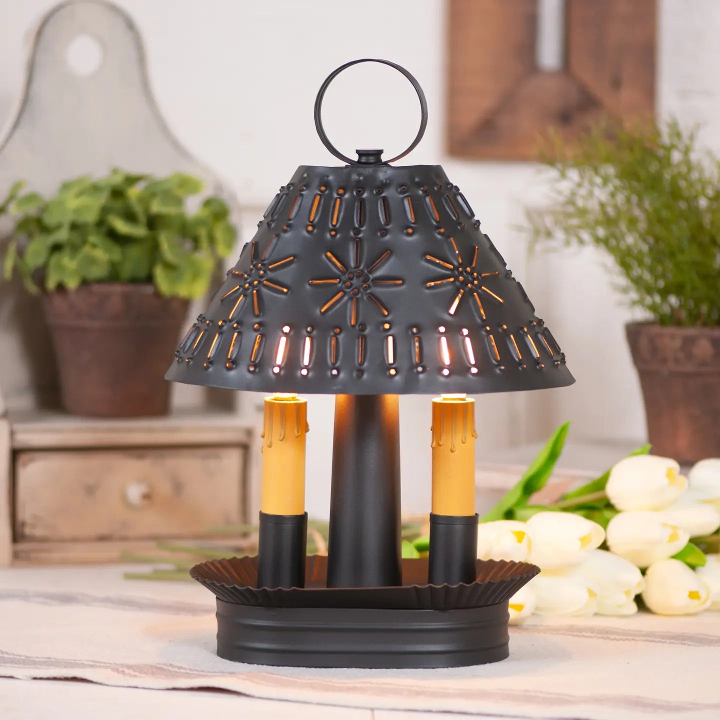 Decorative black lantern with candles on a table, surrounded by plants and flowers.