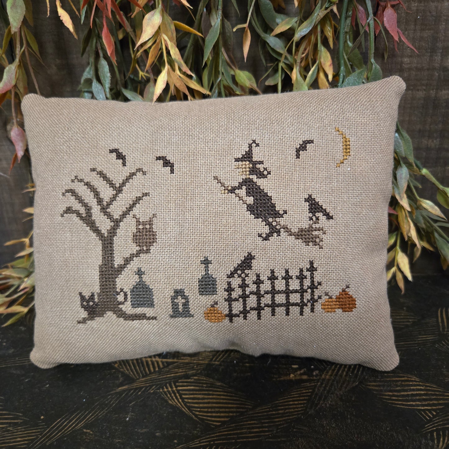 Decorative pillow with cross-stitched design of a cat and bird on a neutral background