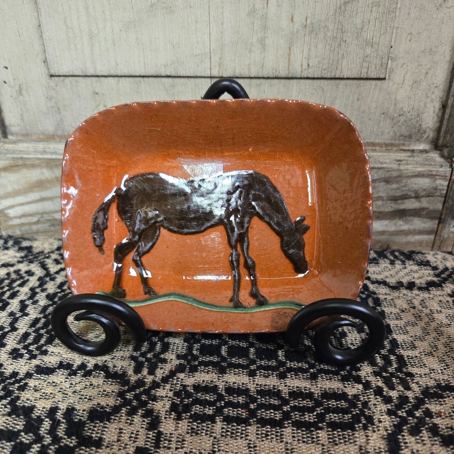 A rectangular ceramic plate with a brown horse, displayed on a wooden surface with a textured black and white background.