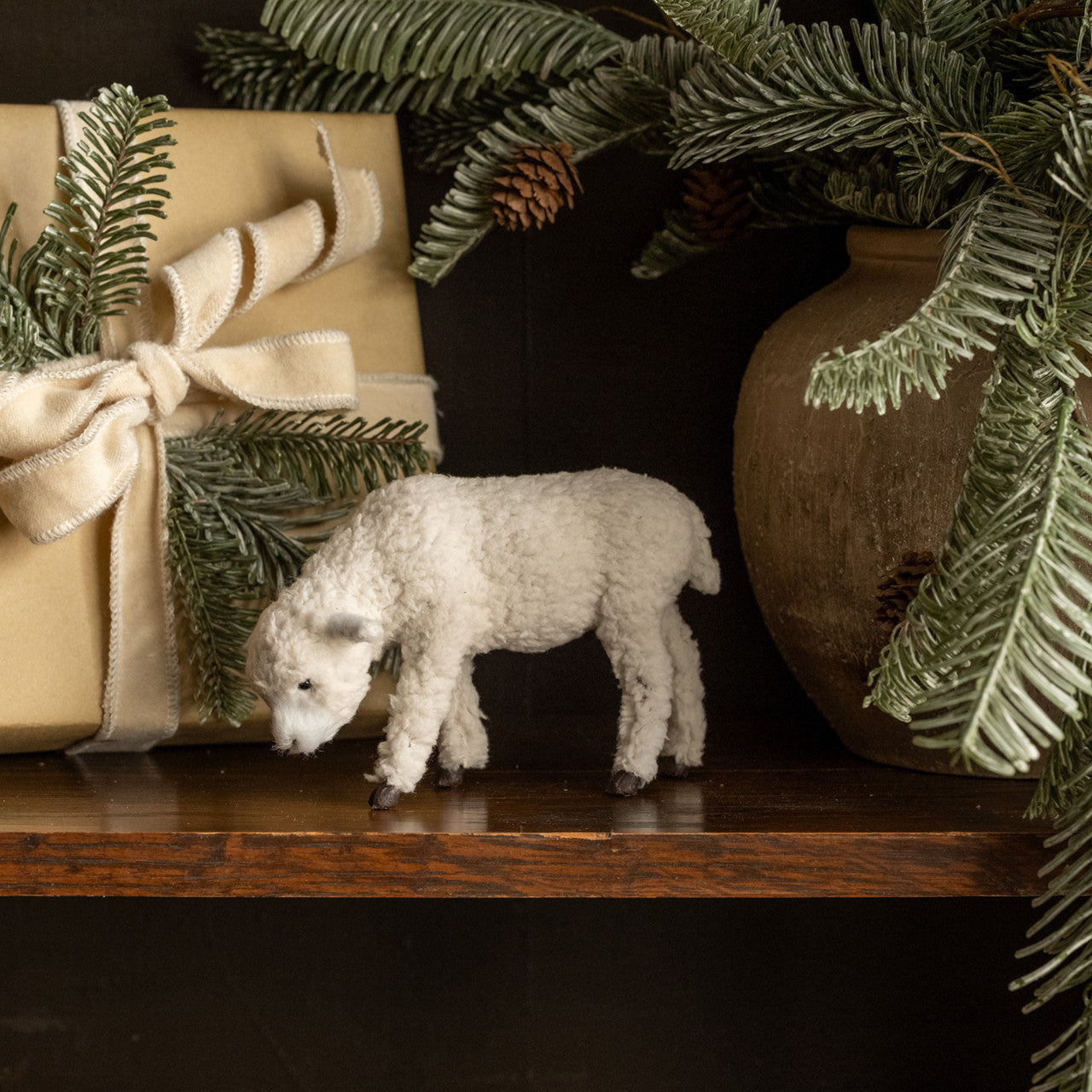 Small white sheep figurine on a wooden surface with Christmas decorations in the background.