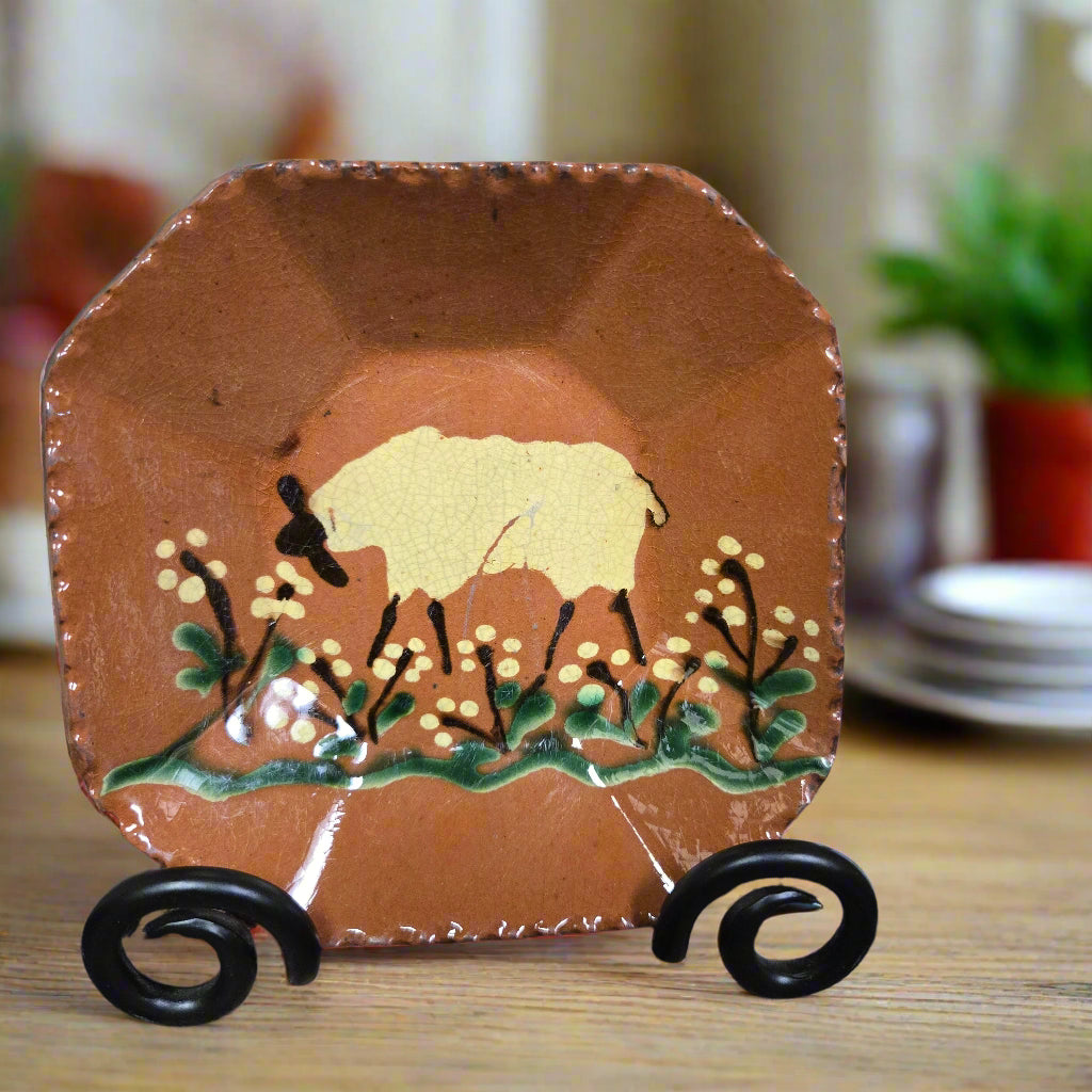 Decorative redware plate with a sheep design on a stand