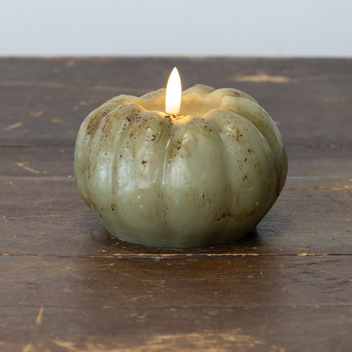 Lighted candle inside a textured green pumpkin on a wooden surface
