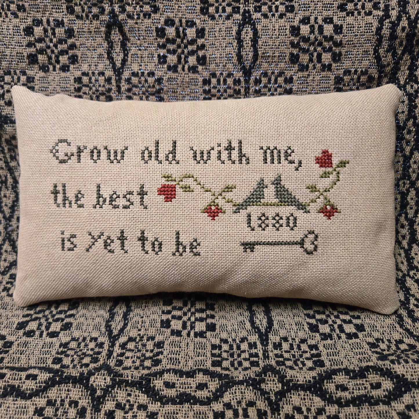 Decorative pillow with cross-stitched design and text on a patterned fabric background