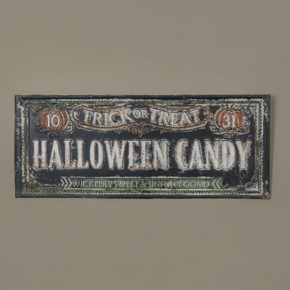 A rectangular Halloween-themed wall sign with distressed typography reading 'Trick or Treat Halloween Candy' and decorative border details, shown against a plain warm gray wall.