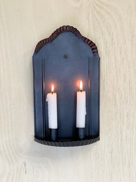 Tin sconce with two white candles displayed on a wood wall.
