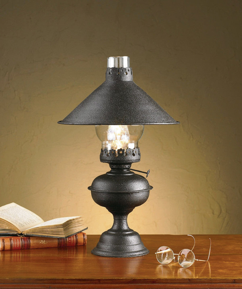 A black oil lamp with a metal shade and glass globe, placed on a wooden surface with an open book and glasses to the side.