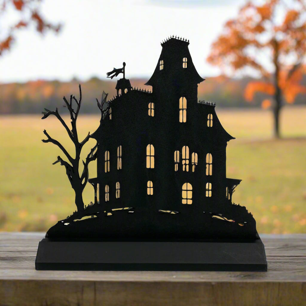 Black silhouette of a haunted house with bare trees on a white background