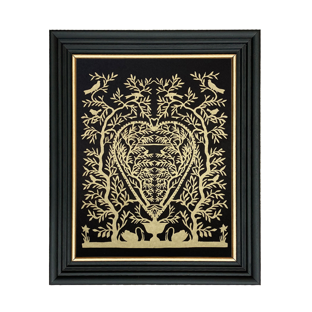 A framed paper cutting artwork featuring a heart-shaped design with swans and trees in gold on a black background, placed against a black frame with a glass cover.