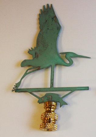 A copper lamp finial with a verdigris finish designed in the shape of a heron in flight.