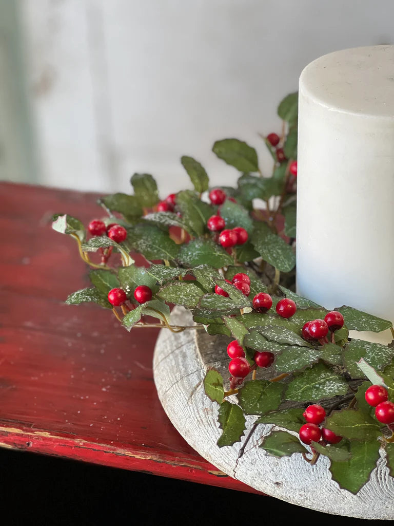 Decorative arrangement with greenery and red berries on a white candle against a blurred background