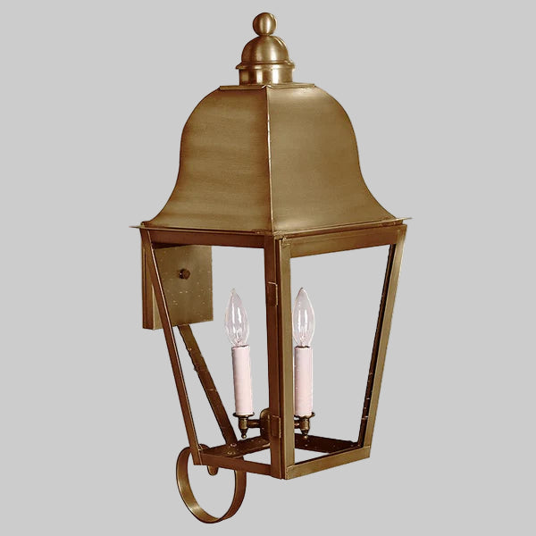 Brass outdoor wall lantern with two lit candles on a gray background