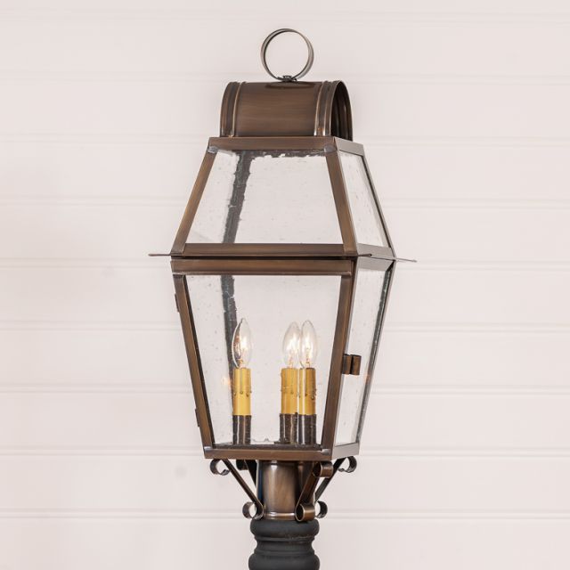 A solid weathered brass outdoor post light with three lights, historic glass, and a blackened solder finish.