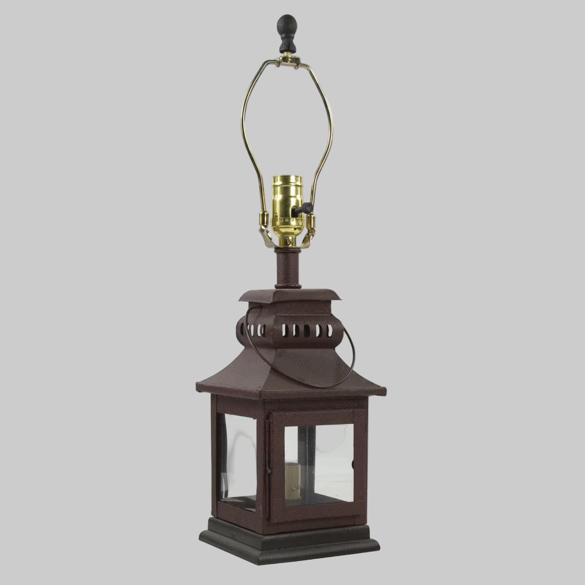 A red iron lantern lamp with a glass shade and a visible wick. It features a knob on the top for adjusting the lighting and a black hook for hanging.
