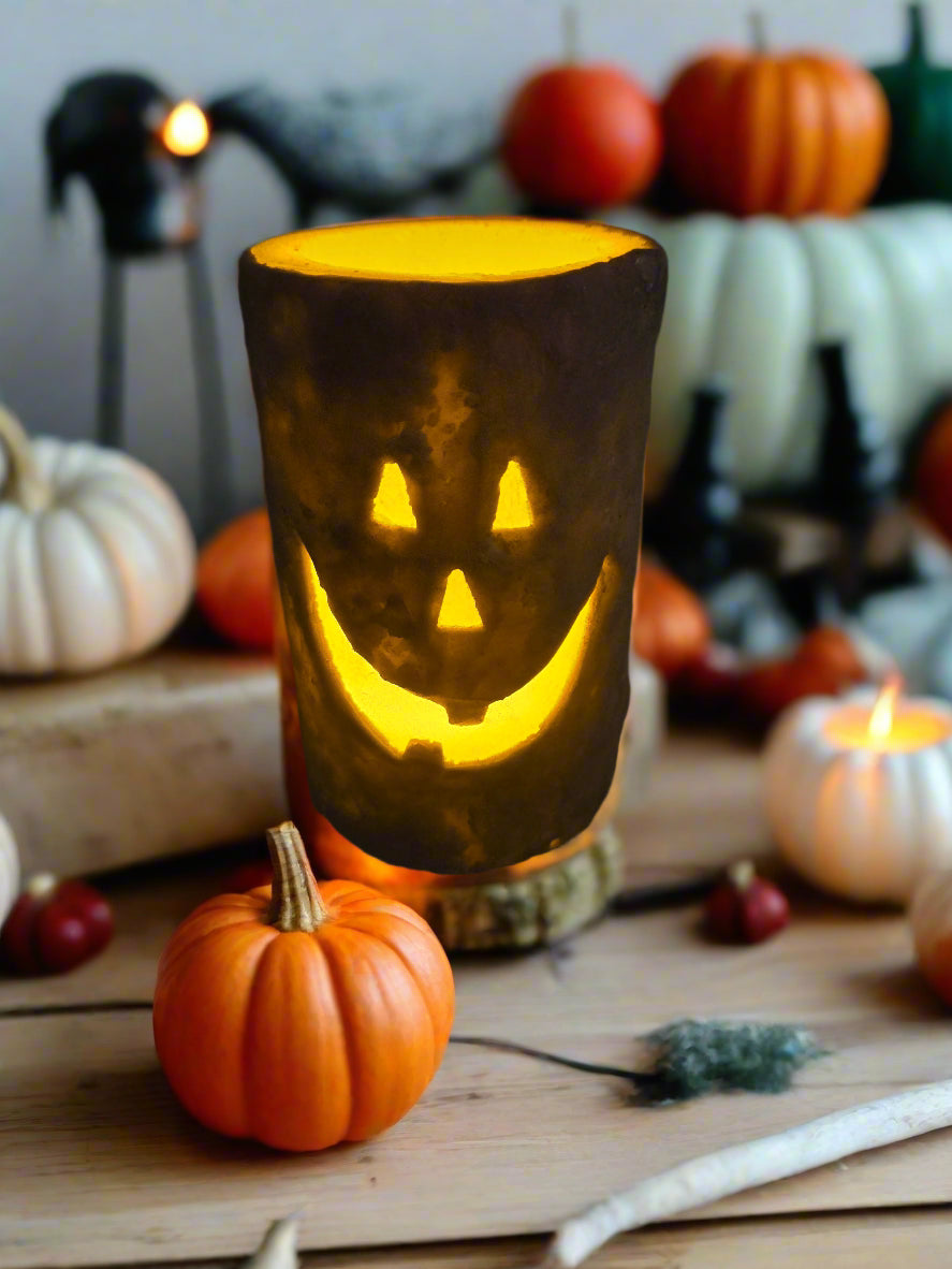 A battery-operated pillar candle with a jack-o'-lantern design, featuring a grungy wax coating and a toothy jack-o'-lantern face pressed into the wax, illuminated from within.