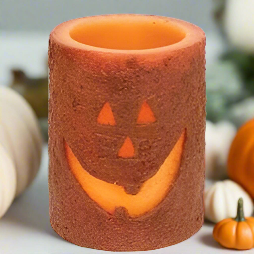 A battery-operated pillar candle with a jack-o'-lantern design, featuring a brown wax coating with a carved face and cinnamon dust.