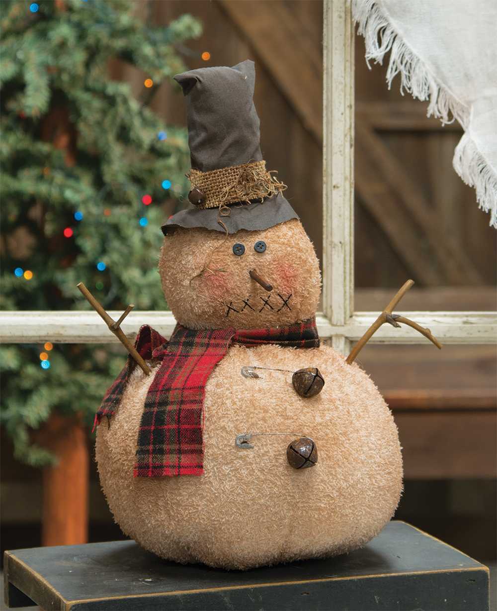 Jingle bell snowman doll with top hat and plaid scarf with stick arms on bench with tree in background