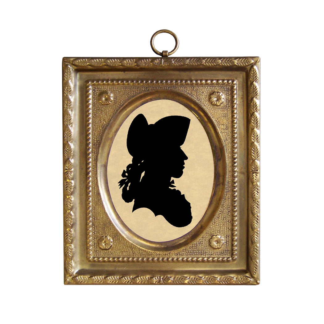 A silhouette of a person wearing a hat, enclosed in an embossed brass frame with a fabric backing, hanging against a white background.