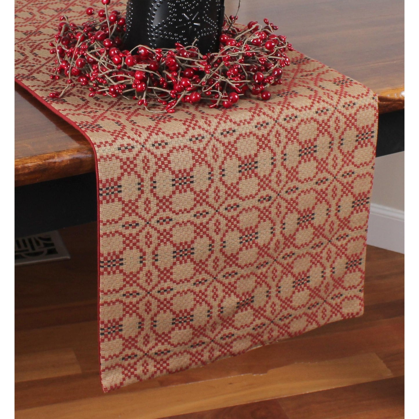 A red and black jacquard table runner with floral patterns, displayed on a wooden table with a decorative piece on top.