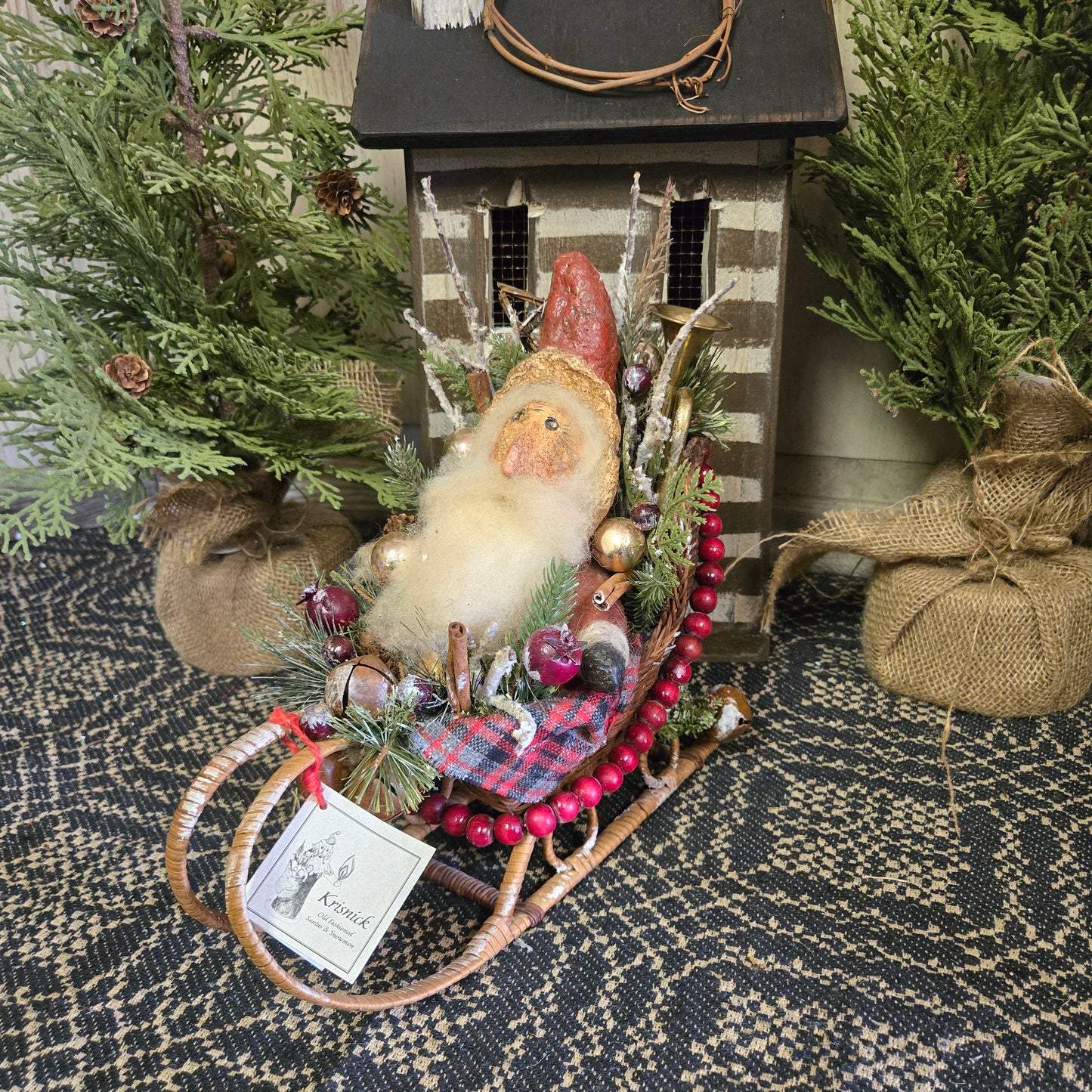 A handcrafted chalkware Santa in a basket sleigh with decorative elements, placed on a patterned surface.