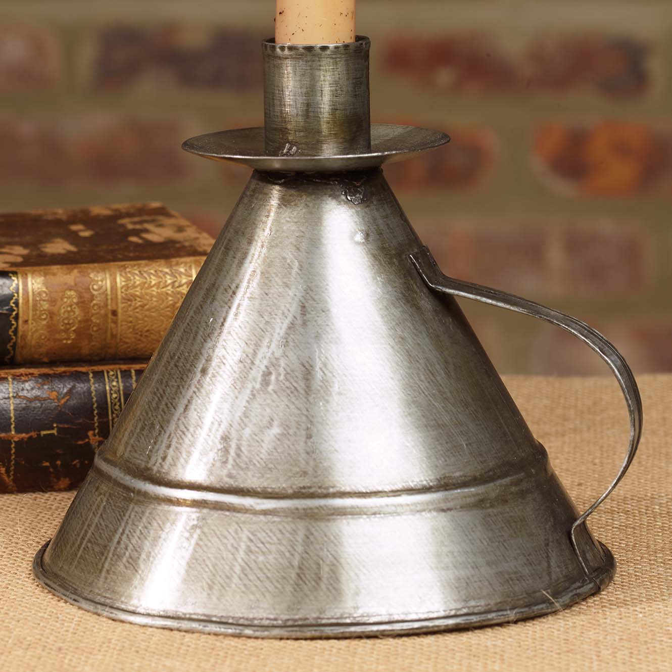 Tin triangular candle holder with a handle sitting next to two books in front of a brick wall