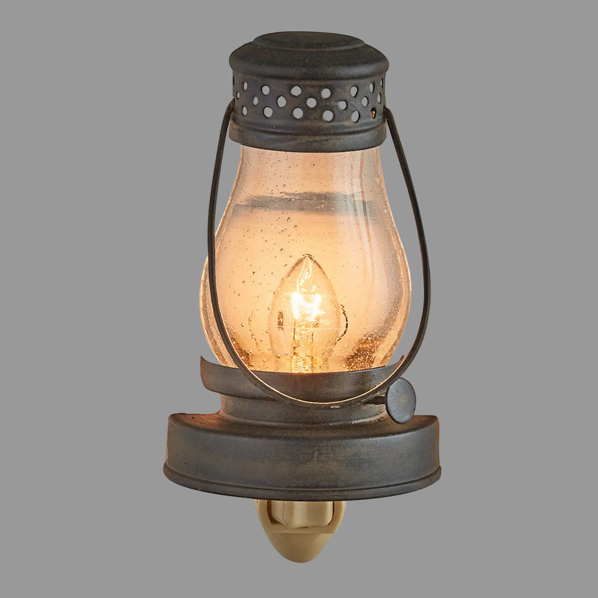 A metal lantern-style night light with a glass diffuser and a lit candle inside, providing a warm glow.