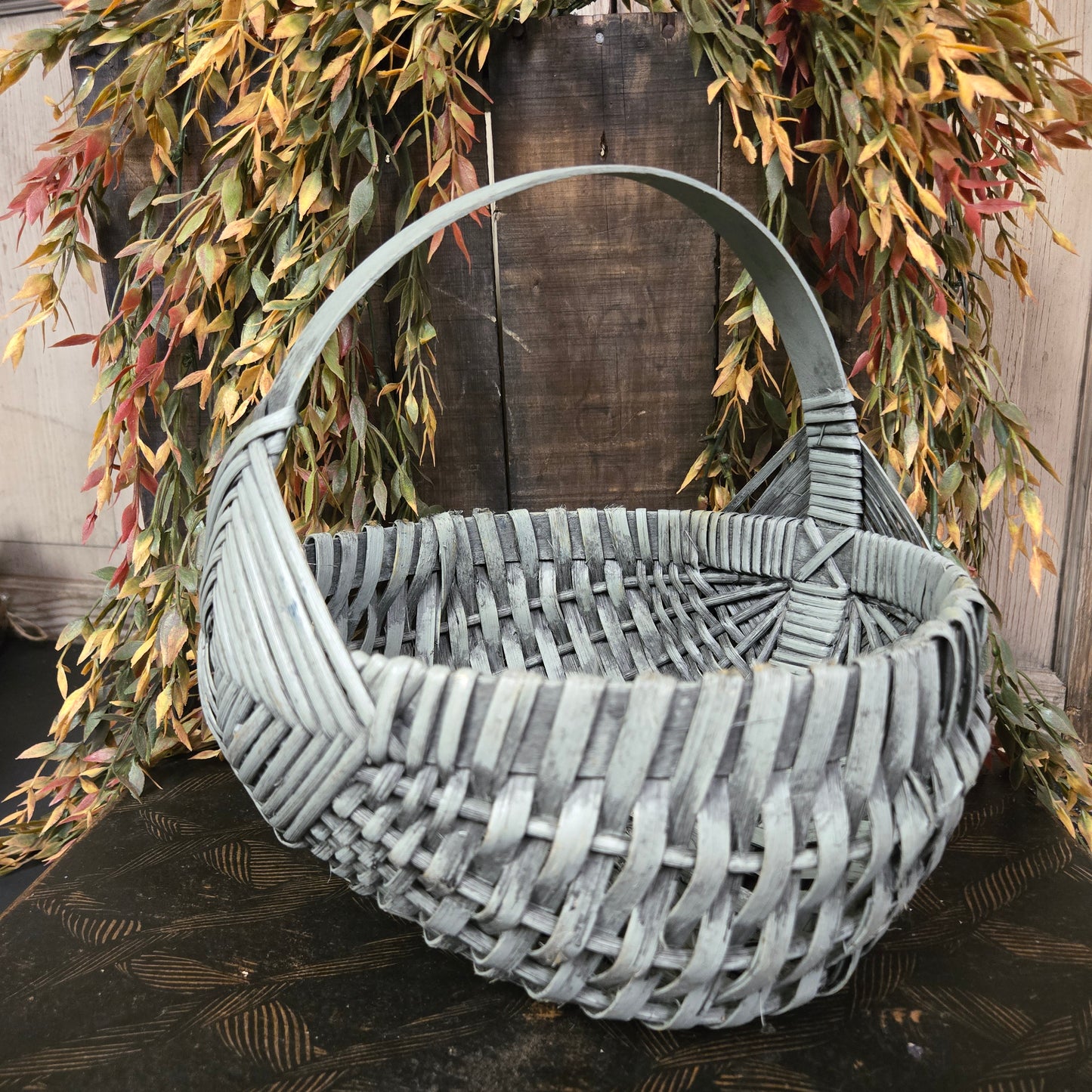 Primitive woven egg basket on a wooden surface with greenery