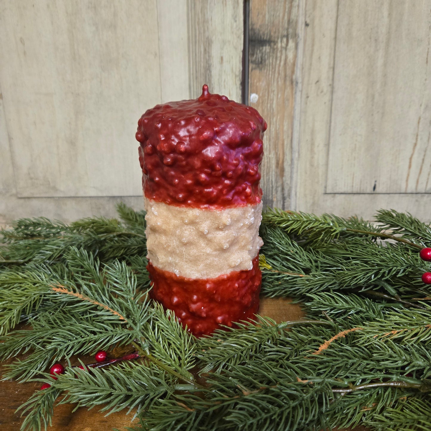 A tall pillar candle with red and cream layers surrounded by Christmas greens