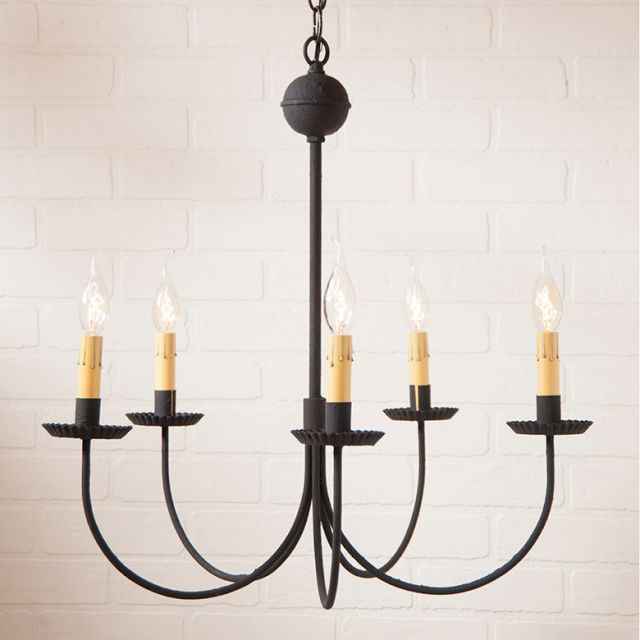 A textured black chandelier with five hanging arms and multiple candle-like light fixtures on each arm, suspended against a white brick wall background.