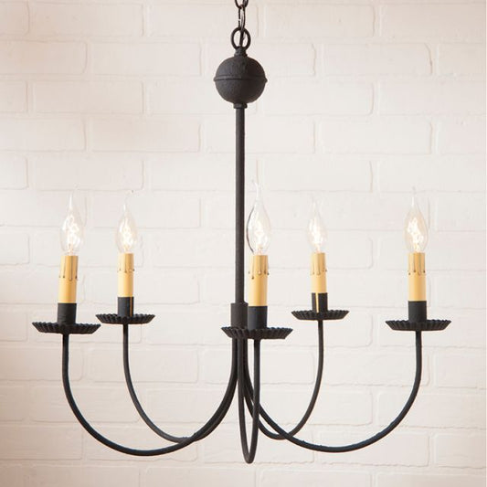 A textured black chandelier with five hanging arms and multiple candle-like light fixtures on each arm, suspended against a white brick wall background.