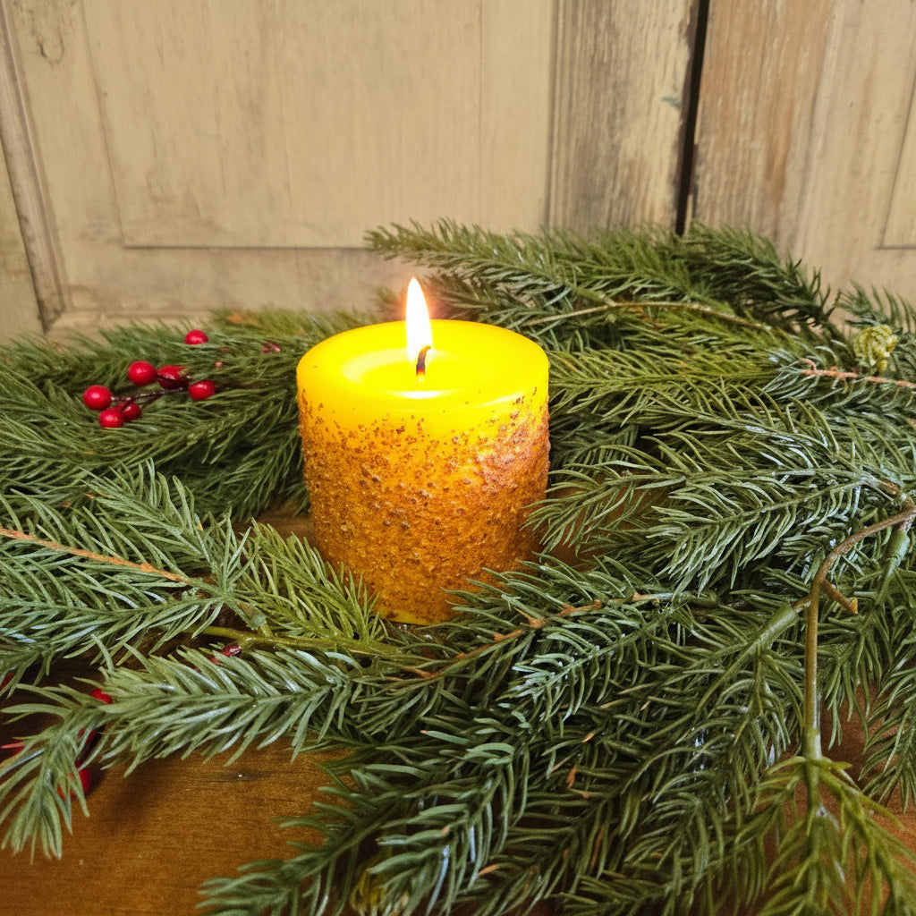 Yellow candle on a bed of greenery with red berries against a wooden background