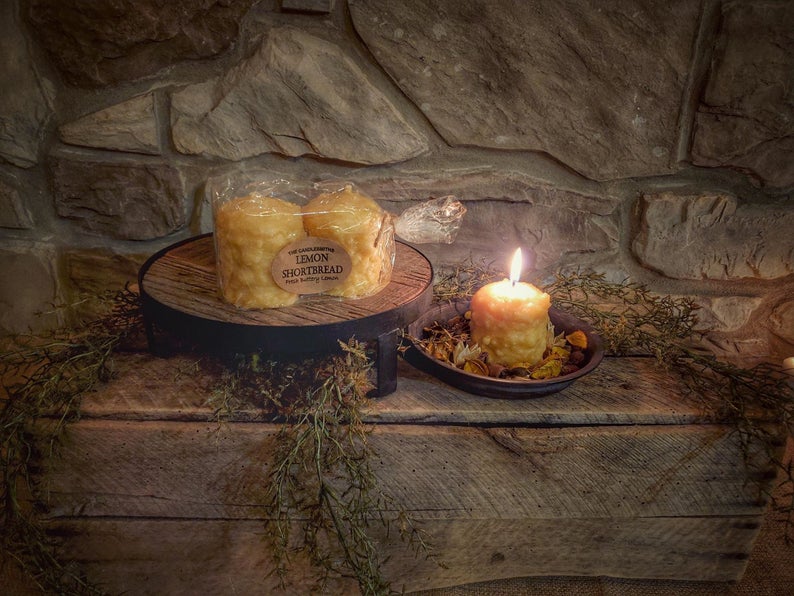 Two lemon-colored votive candles on a wooden surface with a warm light glow, suggesting a fresh lemon fragrance with tones of butter cream and baked shortbread.