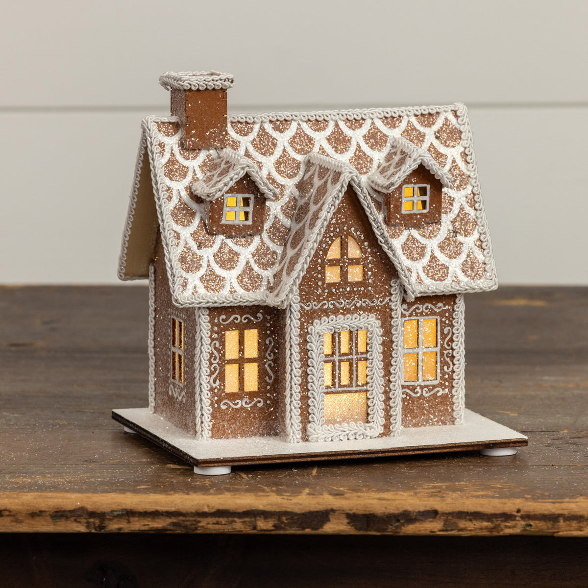 Decorative gingerbread house with lit windows on a wooden surface